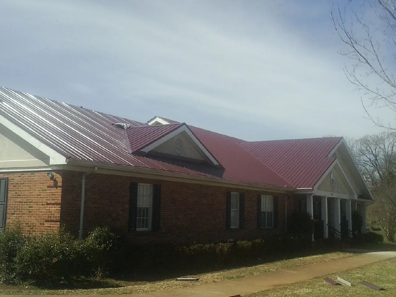 Red metal roof with gabled entries on a long brick building, from a Hail Damage Roof Repair job in Weatherly