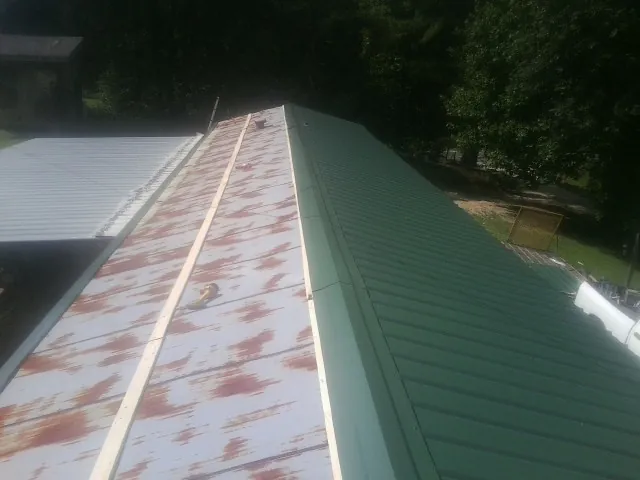 Old rusted panels beside newly installed green metal roofing — Wind Damage Roof Repair by Roofing Brothers in Weatherly