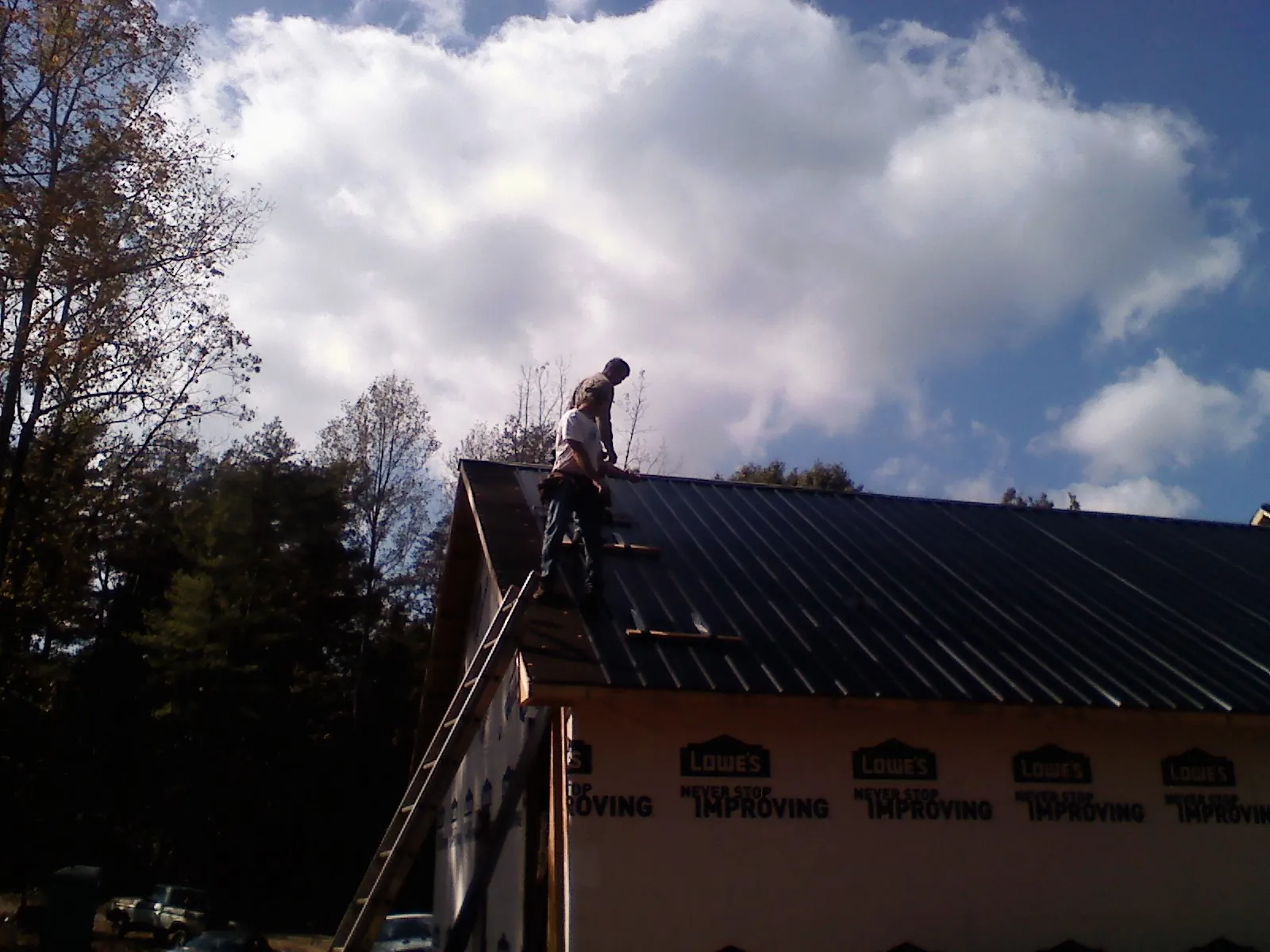 Roofer fastening dark metal panels high against a cloudy sky, from a Roof Inspection job in Weatherly