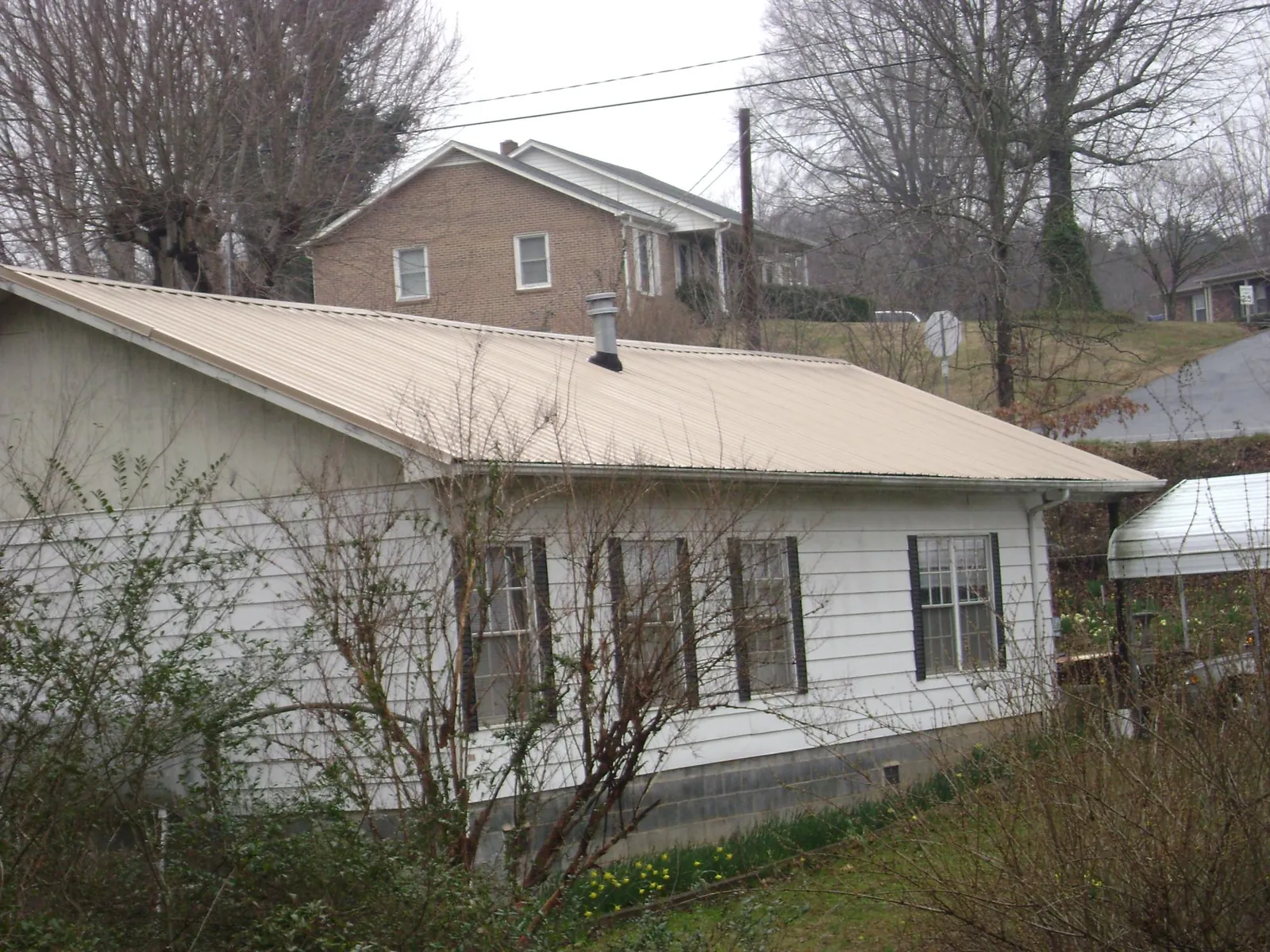 Tan metal roof on a white sided house set into a hillside — Commercial Roofing by Roofing Brothers in Weatherly
